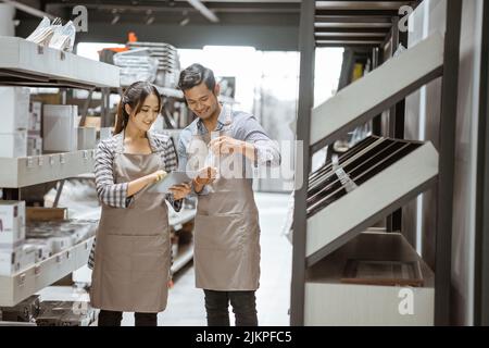 Mann und Frau tragen Schürzen und benutzen ein Polster zwischen den Regalen Stockfoto