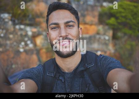 Ich liebe es, im Freien zu fotografieren. Ein junger Mann, der beim Wandern eine Pause einnimmt, um ein schnelles Selfie zu machen. Stockfoto