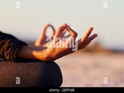 Balancieren meiner Chakren durch Meditation. Eine unkenntliche Frau sitzt allein und meditiert am Strand bei Sonnenuntergang. Stockfoto