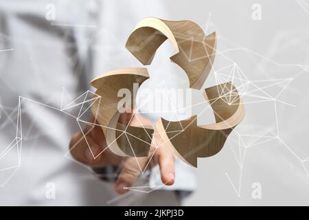 Ein Mann zeigt auf ein schwebendes braunes Recycling-Symbole vor einem verschwommenen Hintergrund Stockfoto