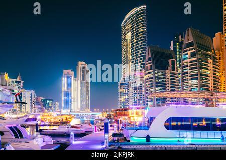 Nachtansicht des Wolkenkratzers in Dubai Marina und Boote, Yachten, die in der Nähe des Pier in der Abendnacht festgemacht wurden Stockfoto