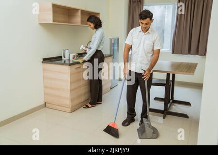 Männlicher Hausmeister, der beim Putzen fegt, und weiblicher Hausmeister, der wischte Stockfoto