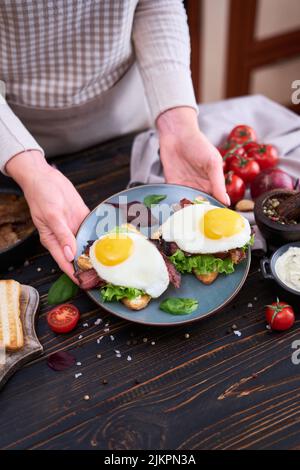 Spiegeleier, Speck und Frischkäse-Sandwiches auf einem Teller auf einem Holztisch in der heimischen Küche Stockfoto