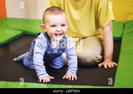 Fröhliches Kleinkind Baby springt mit seiner Mutter im Spielzimmer auf ein Trampolin. Kind im Alter von einem Jahr Stockfoto