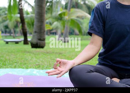 Nahaufnahme eines Halbkörpers einer asiatischen Frau, die morgens im öffentlichen Park Yoga praktiziert, um den Körper stärker zu machen und gegen Krankheiten immun zu sein Stockfoto