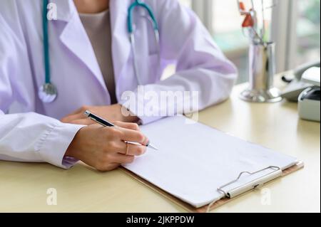 Nahaufnahme eines Arztes, der am Tisch sitzt und Notizen in der Krankenakte macht Stockfoto