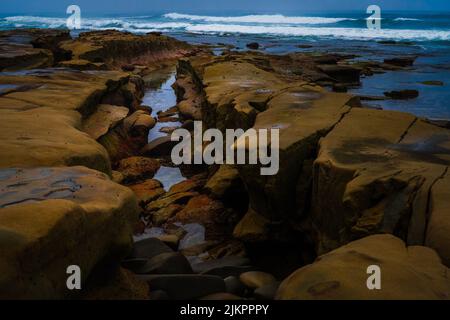 DIE FELSIGE KÜSTE IN LA JOLLA CALIFORNIA MIT WASSER, DAS SICH DURCH DIE FELSEN BEWEGT, MIT EINER SCHÖNEN REFLEXION UND WELLEN, DIE AN DIE KÜSTE KOMMEN. Stockfoto