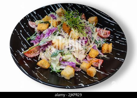 Salat mit Fleisch, Croutons und Gemüse. Schwarzer Teller mit Salat auf weißem Hintergrund. Isolieren. Stockfoto