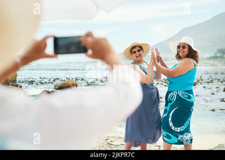 Den Moment und die Erinnerung festhalten. Zwei reife Freunde stehen und posieren für ein Bild während eines Tages am Strand. Stockfoto