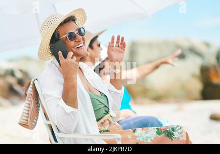 Wir hatten den besten Tag hier. Eine reife Frau saß allein und benutzte ihr Handy während eines Tages am Strand mit Freunden. Stockfoto