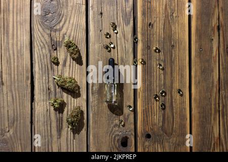 Medizinisches cbd-Öl in einer Glasflasche mit einer Pipette, umgeben von trockenen Marihuanaknospen und cbd-Extrakt in Kapseln. Auf einem hölzernen Hintergrund. Blick von der Stockfoto