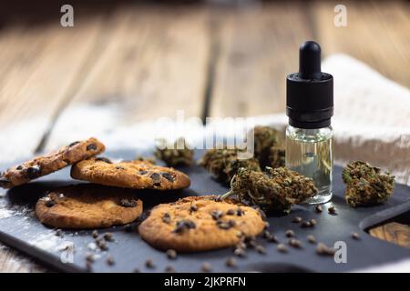 Hausgemachte Chocolate Chip Cookies mit cbd-Öl, umgeben von trockenen Cannabisknospen, Marihuanasamen und einer Glasflasche mit einer Pipette CBD-Öl. Auf ein sto Stockfoto