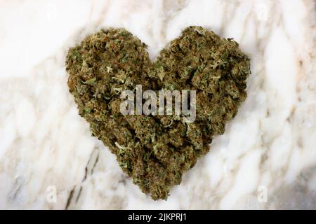 Getrocknete Knospen von medizinischem Marihuana liegen in Form eines Herzens auf einem Marmorboden Stockfoto