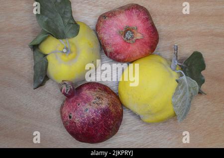 Eine Nahaufnahme von zwei Quitten und zwei Granatäpfeln auf einer Holzoberfläche Stockfoto