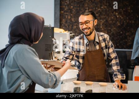 Der Barista nimmt im Café von einer Kundin die Bestellung auf Stockfoto