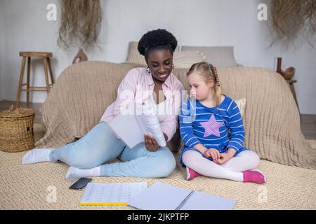 Dunkelhäutige Frau, die einem Mädchen mit Down-Syndrom etwas vorliest Stockfoto