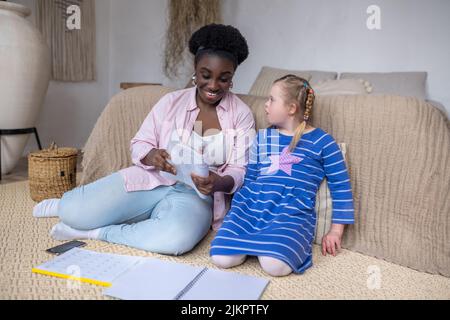 Dunkelhäutige Frau, die einem Mädchen mit Down-Syndrom etwas vorliest Stockfoto