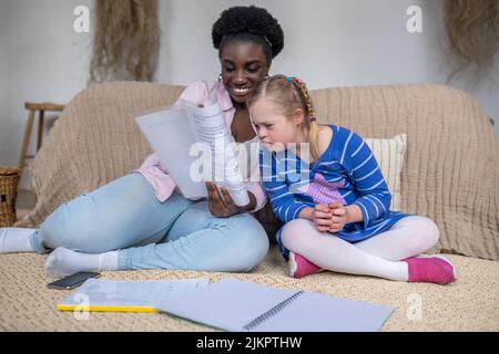 Dunkelhäutige Frau, die einem Mädchen mit Down-Syndrom etwas vorliest Stockfoto