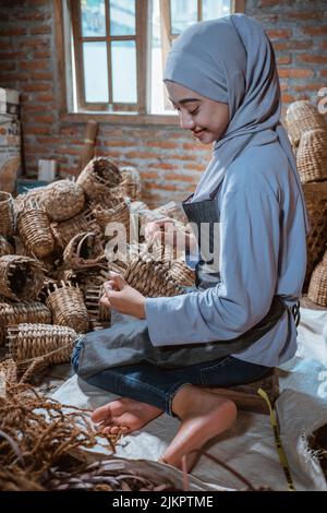 Verschleierte Wasserhyazinthe Handwerkerin sitzt auf dem Boden und webt Kunsthandwerk Stockfoto