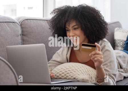 Zahltag. Eine junge Frau, die online einkaufen, während sie zu Hause auf der Couch liegt. Stockfoto