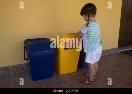 Bild eines entzückenden kleinen Mädchens, das eine Flasche Wasser in eine Mülltonne wirft. Hinweis auf die Erziehung der Kinder zur Achtung der Natur und zur Rezykl Stockfoto