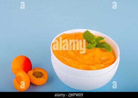 Hausgemachtes veganes Aprikoseneis auf einem Teller auf blauem Hintergrund. Gesundes veganes gefrorenes Dessert. Stockfoto