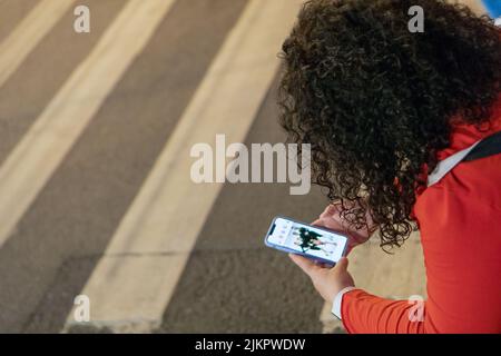 Eine dicke Frau mit langen, lockigen dunklen Haaren in einem leuchtend roten Anzug mit einem Telefon in den Händen sitzt im Zentrum einer europäischen Stadt bei einem cro für Fußgänger Stockfoto