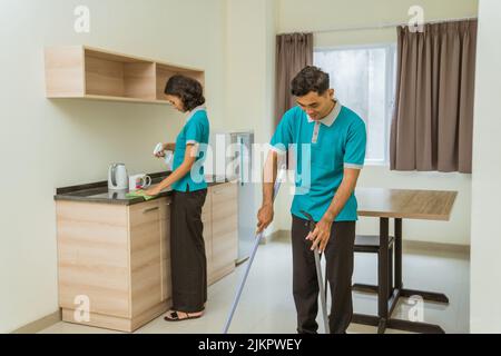 Männlicher Hausmeister in Uniform beim Fegen mit weiblichem Hausmeister beim Wischen Stockfoto