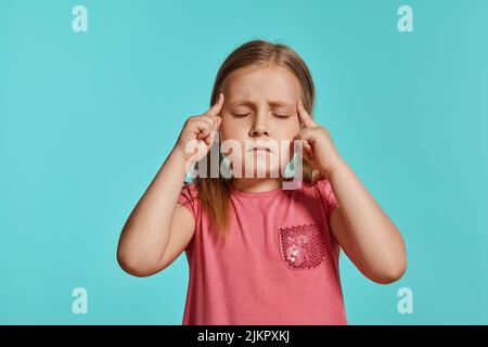 Nahaufnahme eines schönen blonden kleinen Mädchens in einem rosa Kleid, das vor blauem Hintergrund posiert. Stockfoto