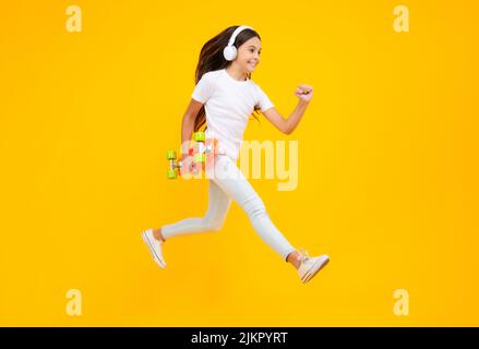 Teen girl 12, 13, 14 Jahre alt mit Skateboard über Studio Hintergrund. Springt und lauft. Cooler moderner Teenager in stilvoller Kleidung. Teenager-Lifestyle Stockfoto