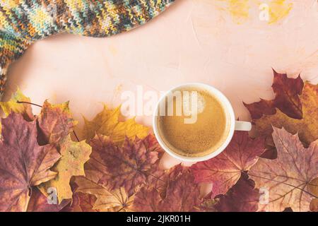 Tasse Espresso mit Crema, Strickpullover und herbstlichen roten Ahornblättern auf rosa Hintergrund. Herbststimmung, flach liegend. Draufsicht, Kopierbereich Stockfoto