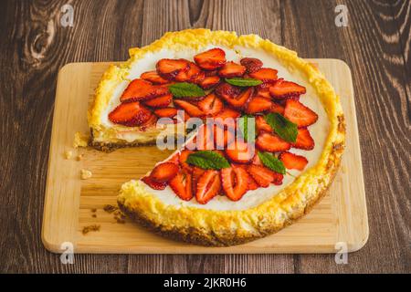 Stück Erdbeer hausgemachten Kuchen auf Holztisch.köstliche Käsekuchen mit Erdbeeren mit Minzblättern verziert.Draufsicht.gesunde Bio-Sommer werden Stockfoto