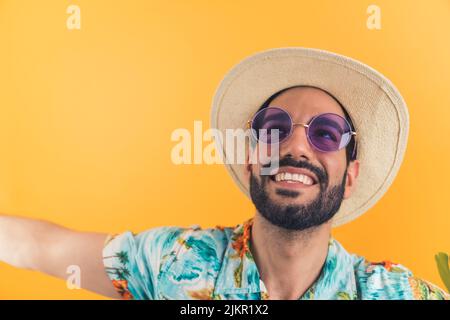 Hispanischer bärtiger Tourist mit Hut und Sonnenbrille freute sich auf den Urlaub und schaute nach oben. Weit gestreckte Arme lächeln. Studioaufnahme. Hochwertige Fotos Stockfoto