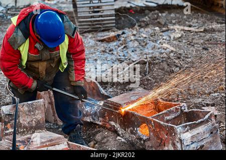 Ein Mitarbeiter im Helm schneidet alte Metallbalken für das Recycling vor Ort Stockfoto