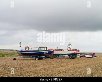 Fischerboote unter einem launischen Himmel am Kiesstrand im Resort Cley, North Norfolk, Großbritannien Stockfoto