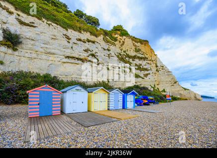Eine Reihe von Strandhütten am Fuße der Kreidefelsen bei Beer, einem kleinen Küstendorf an der Lyme Bay an der Jurassic Coast of East Dorset, Südwestengland Stockfoto