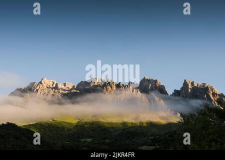 Die Morgenwolken schweben in einem sanften Lichtbild über den felsigen Berggipfeln Stockfoto