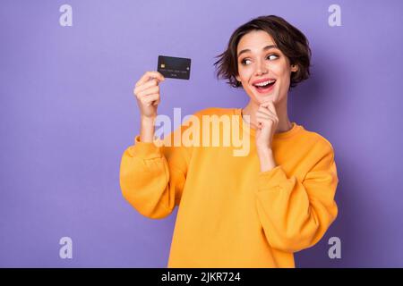 Portrait von attraktiven fröhlich neugierigen Mädchen hält in der Hand Bankkarte Entscheidung isoliert über violett lila Farbe Hintergrund Stockfoto