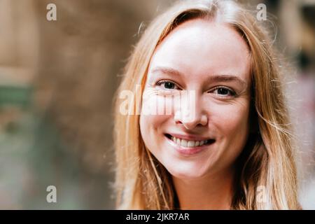 Nahaufnahme eines horizontalen Porträts einer ruhigen und attraktiven jungen blonden Frau. Sie blickt mit einem netten Lächeln auf die Kamera Stockfoto