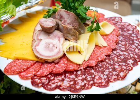 Ein Teller mit kalten Vorspeisen mit verschiedenen Würstchen, Fleisch und Käse. Grünpflanzen und Tomaten Stockfoto