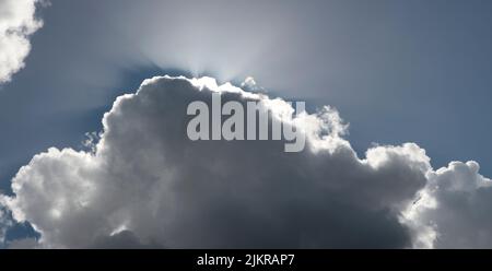 Große graue, schwere Wolke mit Randlicht der Sonne dahinter Stockfoto