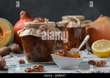 Hausgemachte Kürbiskonfitüre mit Zitrone und Walnüssen in Gläsern und Schüssel auf grauem Hintergrund Stockfoto