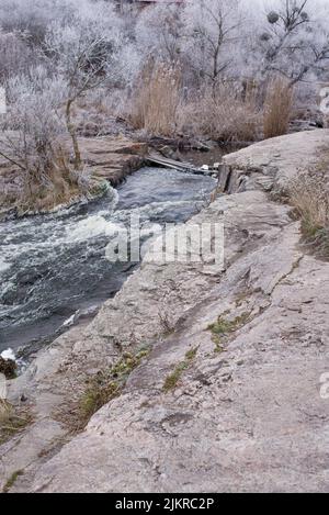 Wunderschöne Winterlandschaft mit dem Fluss Girskiy Tikych, der durch mattierte Bäume und Felsen fließt. Stockfoto