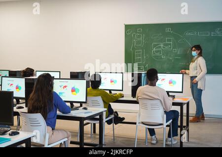 Multirassische Schüler, die während der Business Class Computer mit Sicherheitsmasken in der Schule benutzen - Fokus auf afrikanischem Männerkopf Stockfoto