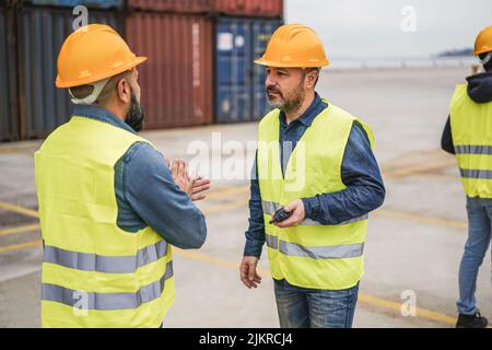 Arbeiter, die Schiffscontainer im Industriehafen im Freien kontrollieren - Fokus auf das rechte Menschengesicht Stockfoto