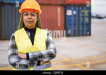 Arbeiter afrikanische ältere Frau lächelt vor der Kamera mit Industriehafen auf dem Hintergrund - Fokus auf Gesicht Stockfoto