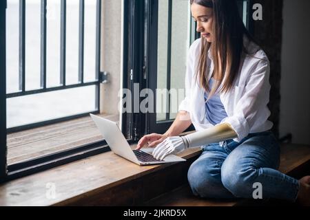 Motivierte Frau mit prothetischen Arm arbeiten Notebook-Computer, Text eingeben, Mädchen mit Behinderung führt normales Leben künstliche Prothese Extremität, Menschen Stockfoto