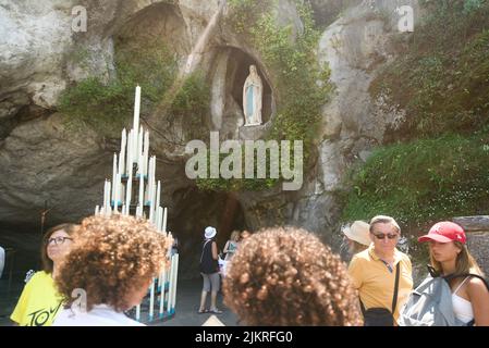 Die Menschen versammelten sich in der Grotte von Massabielle/Grotte der Erscheinungen in der Wallfahrtskirche unserer Lieben Frau von Lourdes, Wallfahrt. (Statue der Jungfrau Maria in der Grotte) Stockfoto