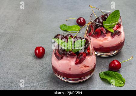Köstliche italienische Dessert-Panna Cotta mit süßer Kirschsauce, frischen Beeren und Minzblättern. Stein Beton Hintergrund, kopieren Raum Stockfoto