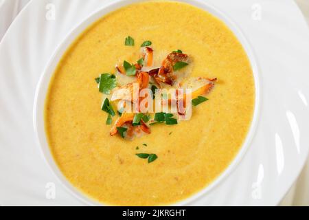 Cremige Suppe aus Pfifferlingen in einer weißen Schüssel auf einem weißen Holztisch, Nahaufnahme Stockfoto